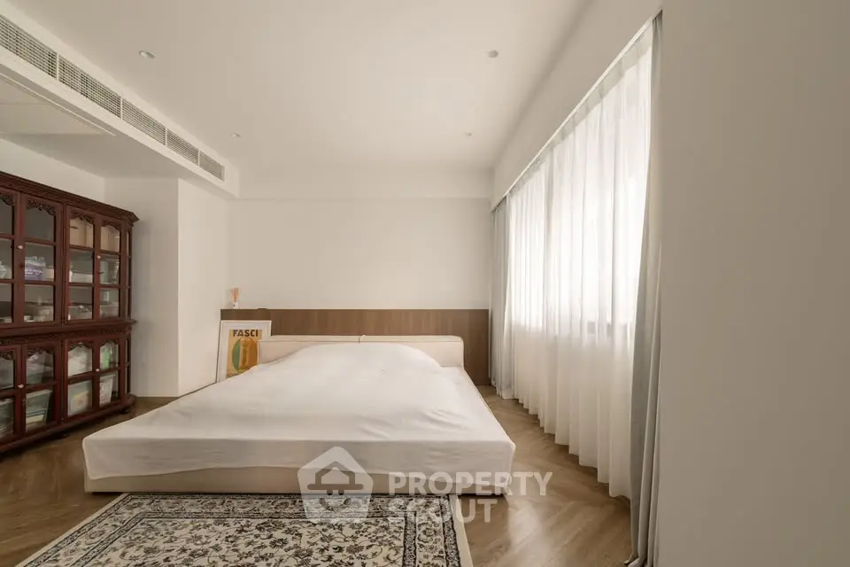 Spacious bedroom with elegant wooden flooring and large window for natural light.