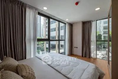 Modern bedroom with large windows and city view, featuring cozy bedding and elegant curtains.
