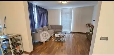 Spacious living room with modern decor and wooden flooring, featuring a cozy gray sofa and large windows.