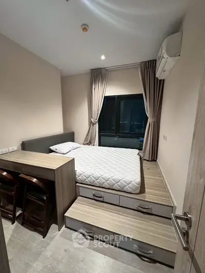 Modern bedroom with elevated bed and storage drawers, featuring a large window with city view.