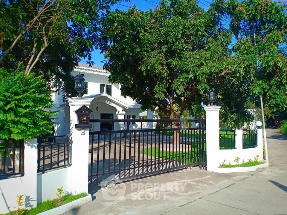 Stunning white villa with lush greenery and gated entrance, perfect for luxurious living.