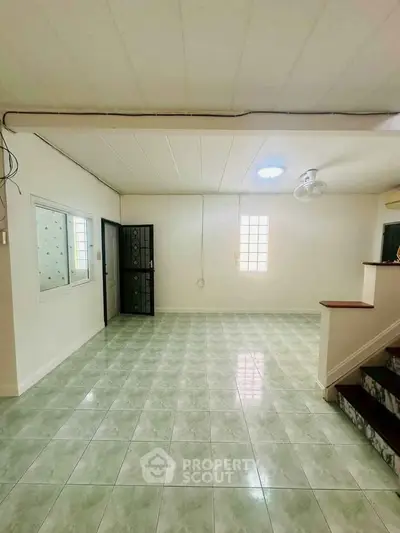 Spacious unfurnished room with tiled flooring and staircase, ideal for customization.