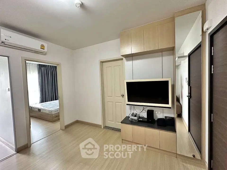 Modern living room with built-in TV unit and view into cozy bedroom