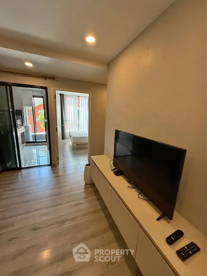 Modern living room with sleek TV setup and wooden flooring, leading to a bright bedroom.