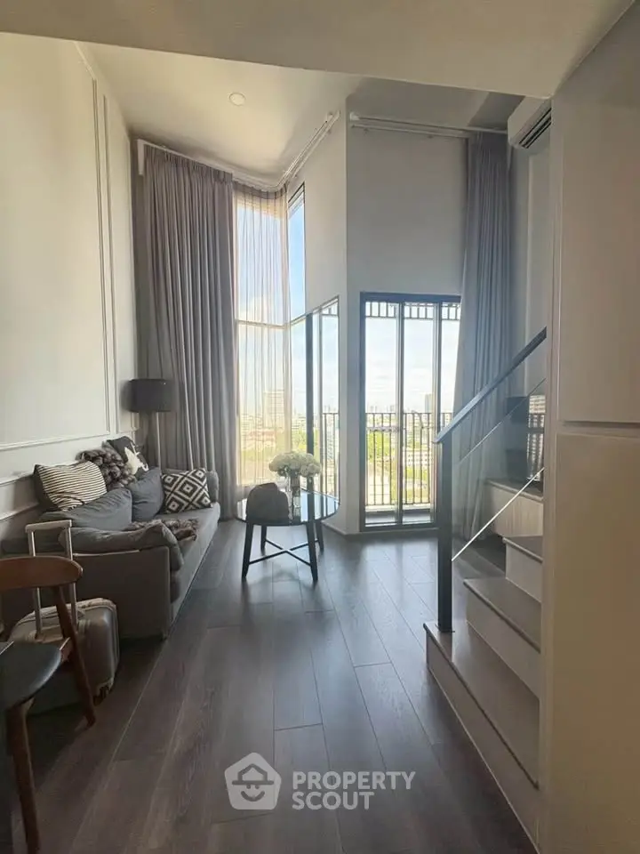 Modern loft-style living room with high ceilings and large windows offering a stunning city view.