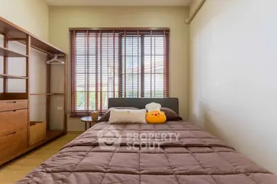 Cozy bedroom with wooden furniture and large window with blinds, perfect for relaxation.