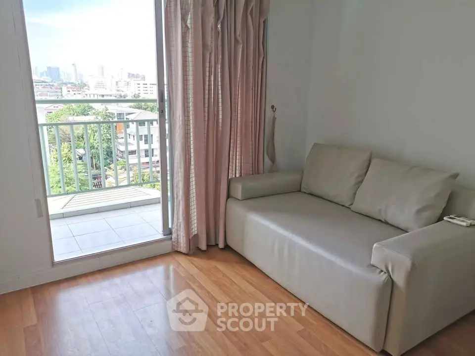 Cozy living room with balcony and city view, featuring a comfortable sofa and wooden flooring.