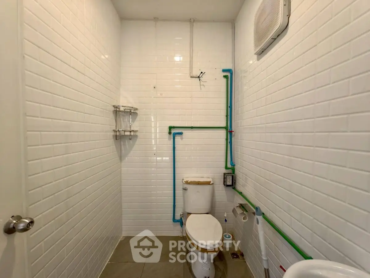 Compact bathroom with white subway tiles and visible plumbing, featuring a modern toilet.