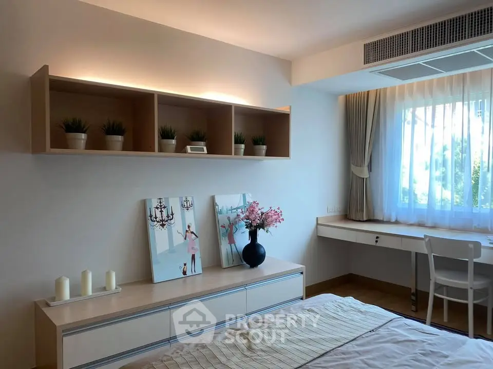 Modern bedroom with stylish decor and natural light, featuring a cozy workspace and elegant shelving.