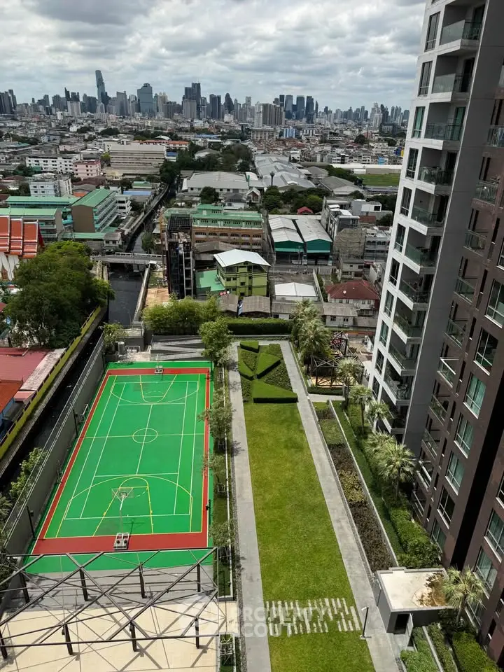 Stunning urban view from high-rise building with sports court and lush green garden.