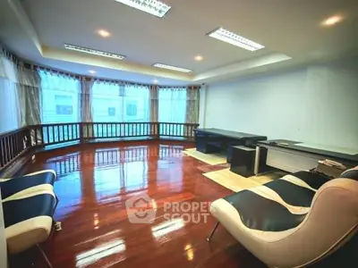 Spacious living room with polished wooden floors and modern furniture, featuring large windows for natural light.