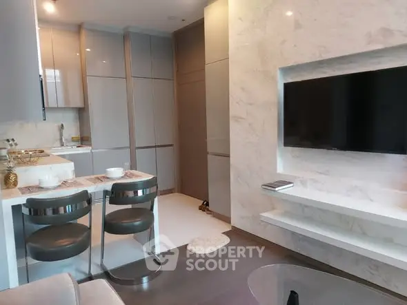 Modern living room with sleek kitchen and wall-mounted TV, featuring elegant marble accents.