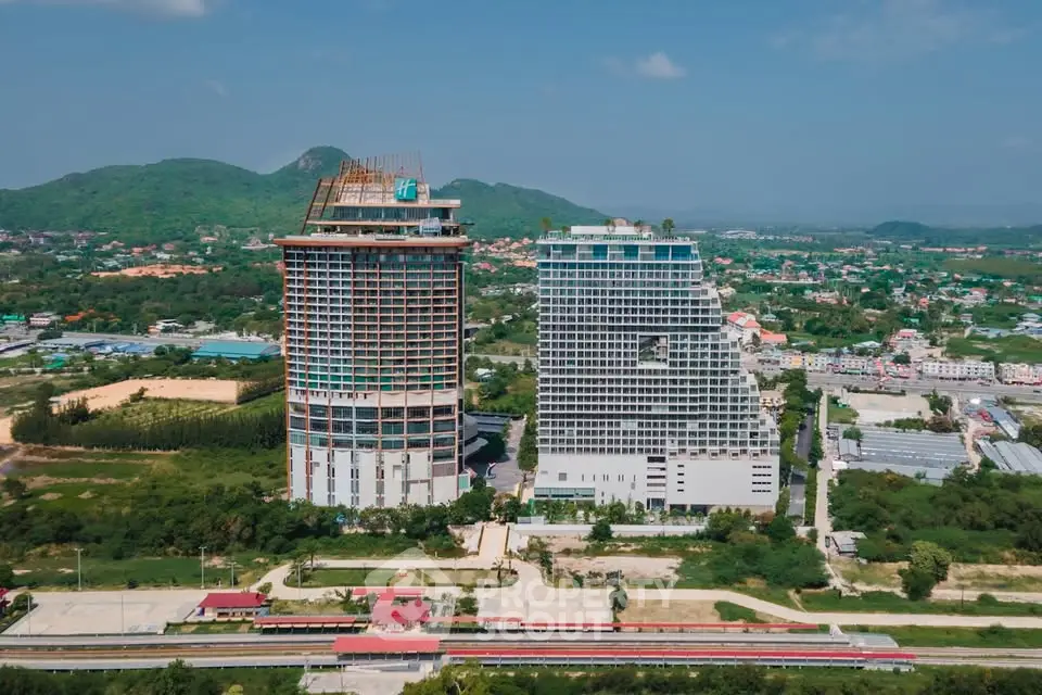 Stunning aerial view of modern high-rise buildings amidst lush greenery and scenic mountains.