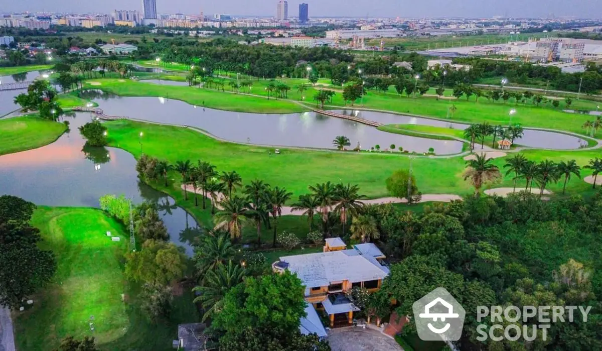 Stunning aerial view of lush green golf course with serene water features and modern cityscape backdrop.