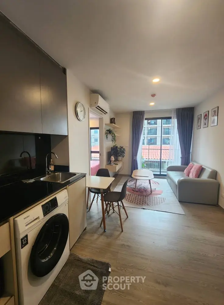 Modern living room with open kitchen and washing machine, featuring stylish decor and natural light.