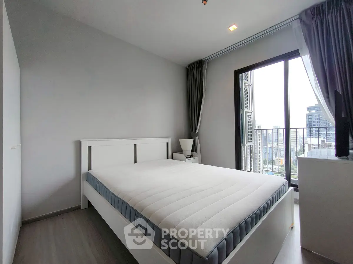 Modern bedroom with city view and balcony access in high-rise apartment.