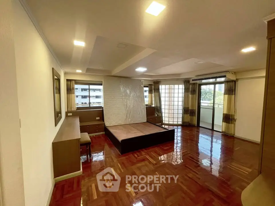 Spacious bedroom with hardwood floors and large windows opening to a balcony, offering ample natural light.