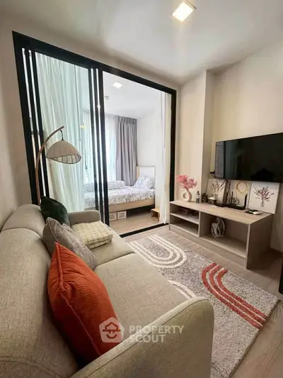 Modern living room with cozy sofa and stylish decor leading to a bright bedroom through glass doors.