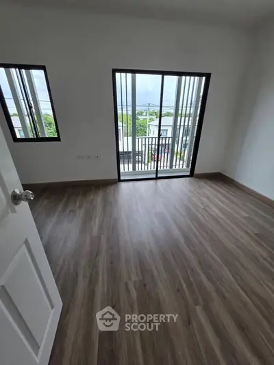 Spacious bedroom with large windows and balcony access, featuring elegant wood flooring.