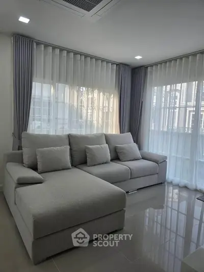 Modern living room with sleek gray sofa and large windows.