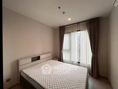 Spacious bedroom with large window and modern furnishings in a high-rise apartment.