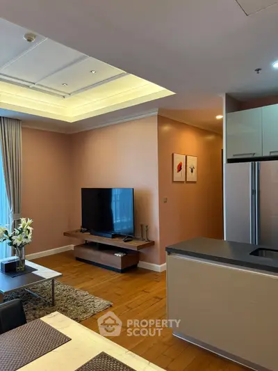 Modern living room with sleek TV setup and open kitchen design, featuring elegant decor and warm lighting.