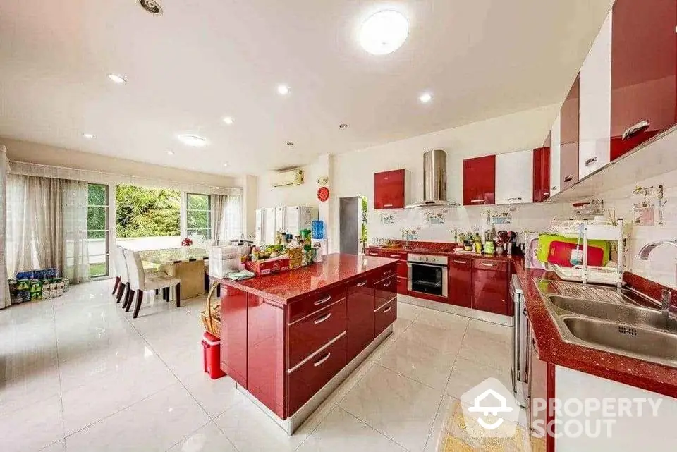 Spacious modern kitchen with red cabinetry and dining area, featuring open layout and natural light.