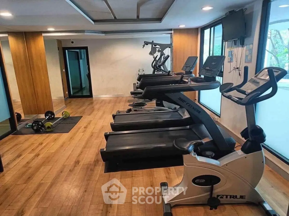 Modern gym with state-of-the-art fitness equipment and wooden flooring in a residential building.