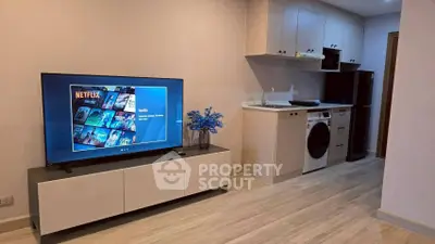 Modern living room with TV and compact kitchen featuring washing machine and fridge.