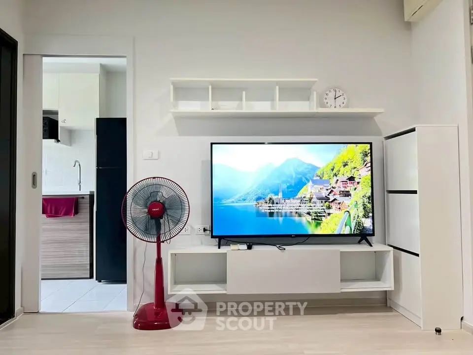 Modern living room with sleek TV setup and stylish fan, adjacent to a compact kitchen area.