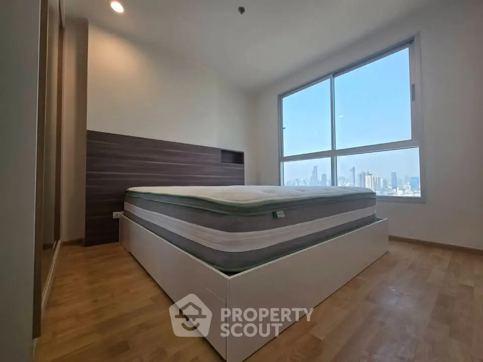 Spacious bedroom with large window offering stunning city skyline views.