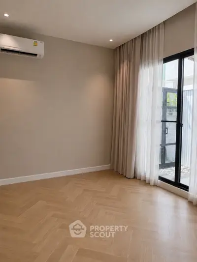 Spacious empty room with elegant wooden flooring and large window for natural light.