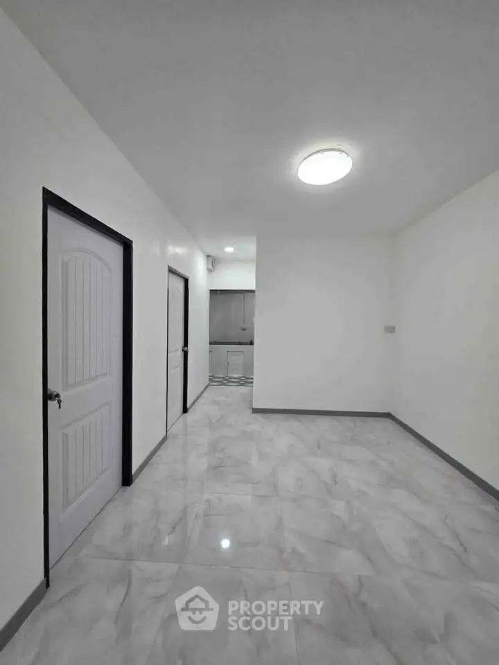 Spacious modern apartment interior with sleek marble flooring and bright lighting, leading to a contemporary kitchen.