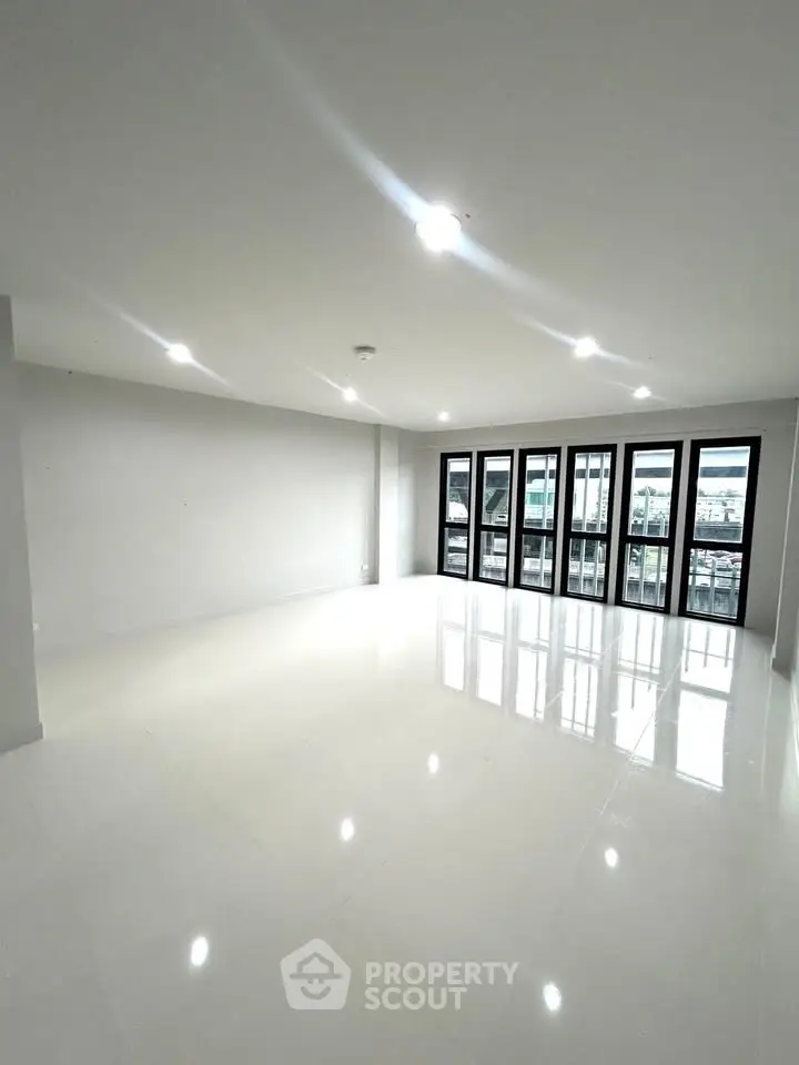 Spacious modern living room with large windows and glossy white flooring, offering ample natural light.