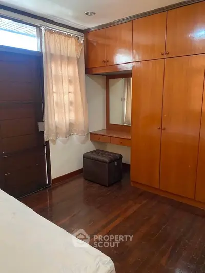 Cozy bedroom with wooden flooring and built-in wardrobe, featuring a vanity area and natural light.