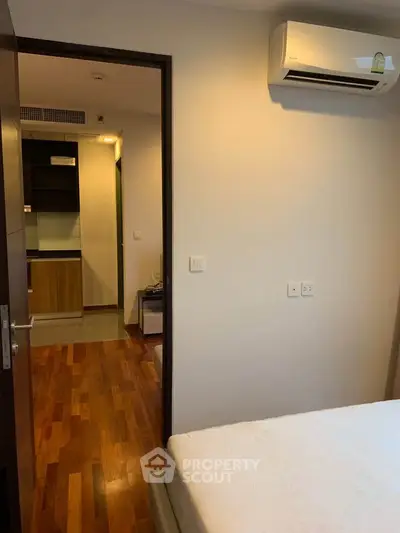 Cozy bedroom with air conditioning and wooden flooring, leading to a modern kitchen area.