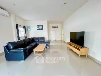 Spacious modern living room with sleek black sofa and large TV, perfect for relaxation and entertainment.