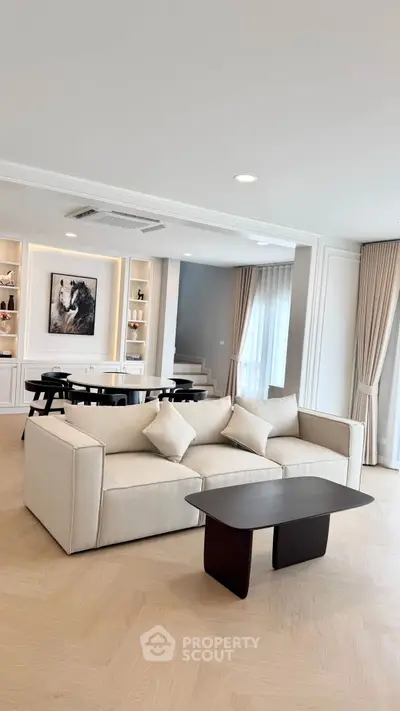 Elegant living room with modern beige sofa, stylish coffee table, and chic dining area in open layout.