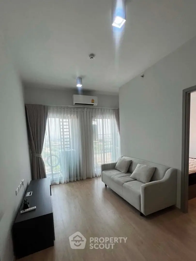 Modern living room with sleek sofa and large window offering natural light and city view.