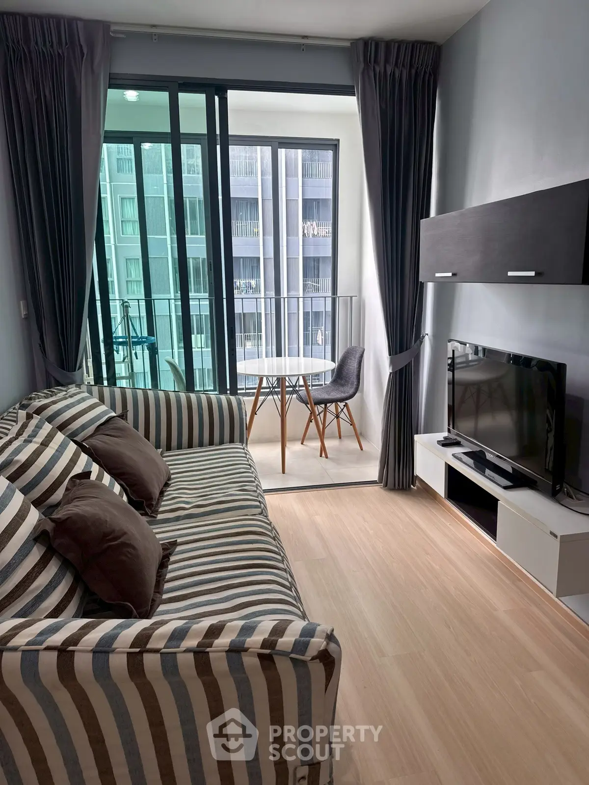 Modern living room with striped sofa, TV, and balcony view in stylish apartment.