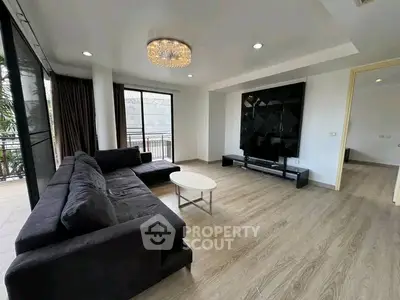 Spacious modern living room with elegant chandelier and large windows opening to balcony.