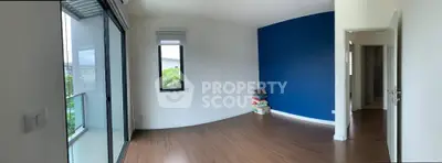 Spacious empty room with wooden flooring and blue accent wall, featuring a balcony view.