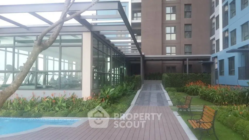 Modern apartment building with lush garden and poolside view, featuring a sleek glass gym area.