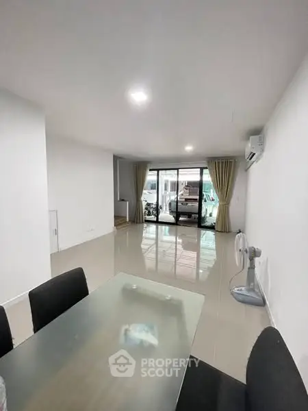 Spacious modern living room with glass table and large windows leading to balcony.