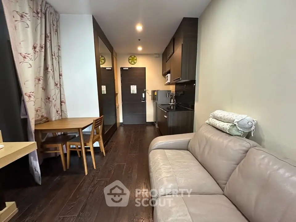 Modern apartment interior with cozy living room and kitchen area, featuring elegant dark wood flooring.