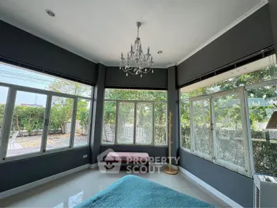 Spacious bedroom with large windows and garden view, featuring elegant chandelier and modern decor.