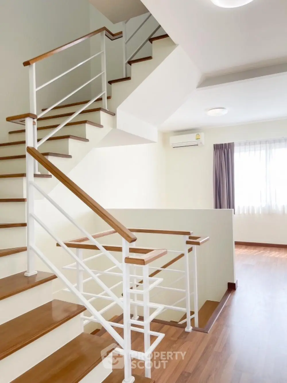 Bright and airy multi-level home interior with elegant wooden staircase, pristine white walls, and warm wooden flooring, perfect for modern living.