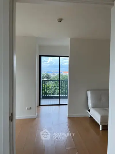 Bright room with wooden floors and balcony view, featuring a modern white sofa.