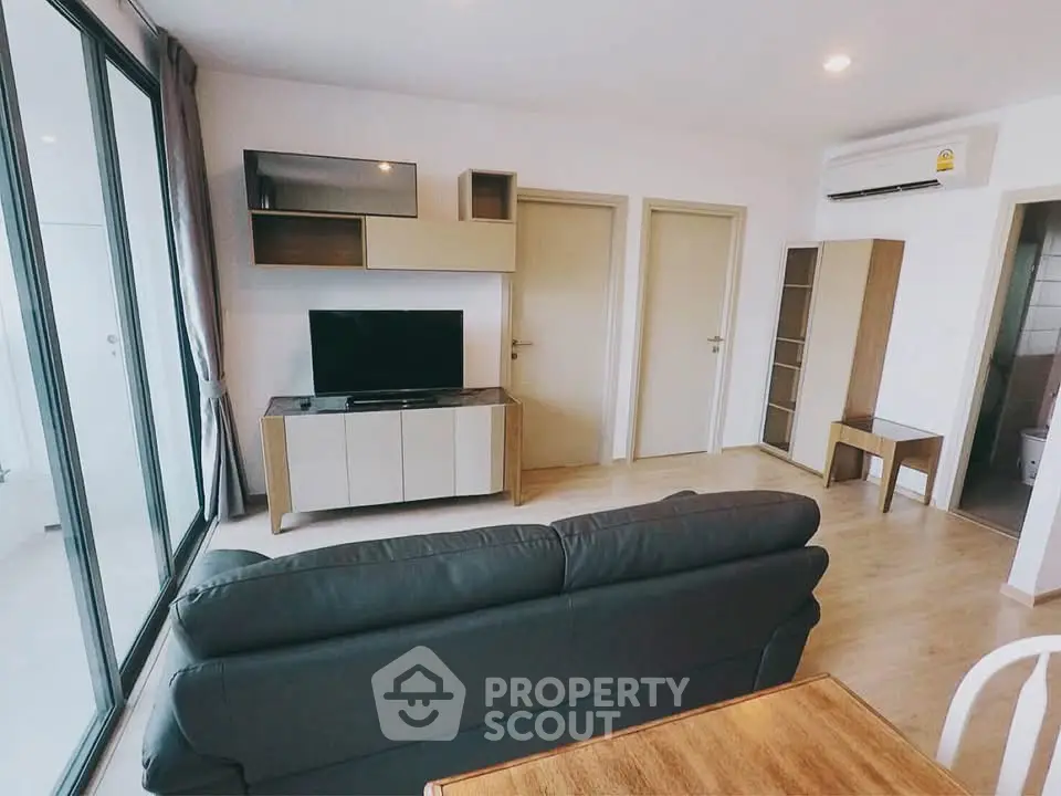 Modern living room with sleek furniture and large glass doors leading to a balcony.