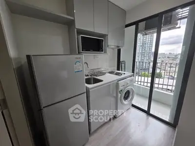 Modern compact kitchen with balcony view, featuring fridge, microwave, and washing machine.